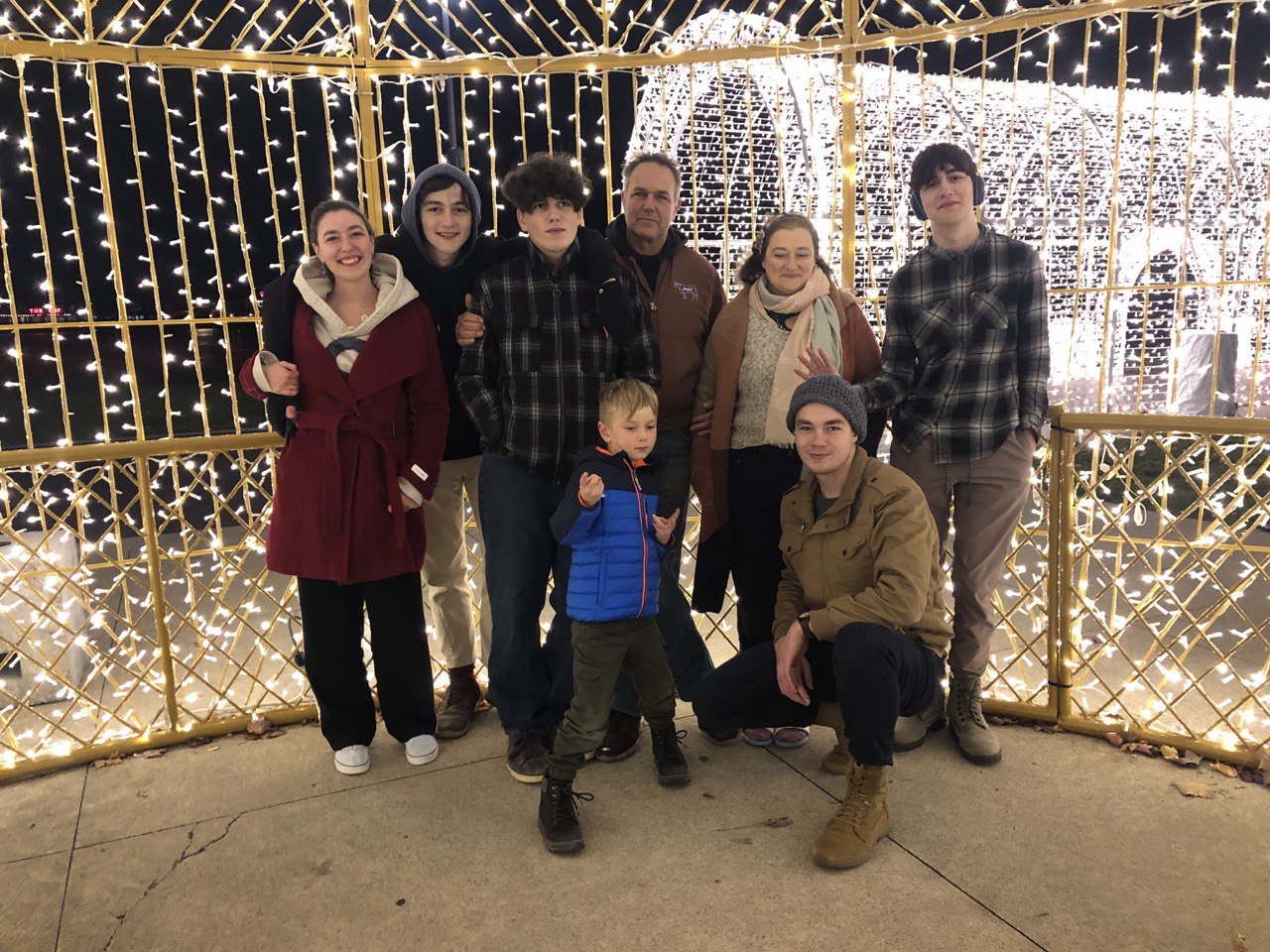 Family picture of my husband and I with our 6 children. Christmas lights in background, and several making goofy faces.